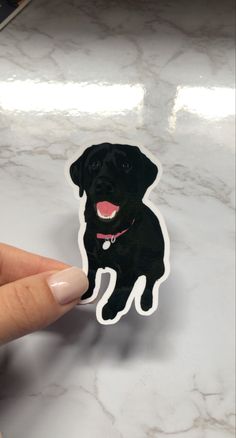 a hand holding a sticker with a black dog on it's face and tongue sticking out