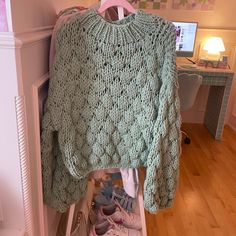 a green sweater hanging up on a rack in a room with shoes and a computer