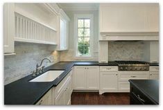 a kitchen with white cabinets and black counter tops is pictured in this image, there are two windows above the sink