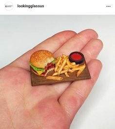 a miniature hamburger and french fries on a small wooden tray with ketchup in it