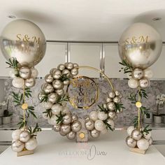 some balloons are sitting on top of a table with silver balls and greenery around them