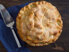 a pie sitting on top of a wooden table next to a knife and fork with a blue napkin