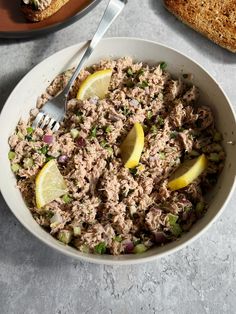 a white bowl filled with tuna salad next to two slices of bread on a table