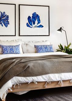 a bed with blue and white pillows in a bedroom next to two pictures on the wall