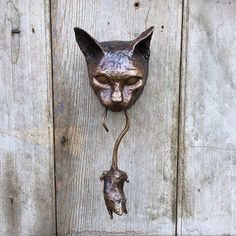 a metal cat head mounted to the side of a wooden door with a rat hanging from it's mouth