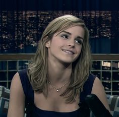 a woman sitting on top of a couch in front of a window with the city lights behind her