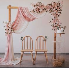 two wooden chairs sitting next to each other under a pink and white drape with flowers on it