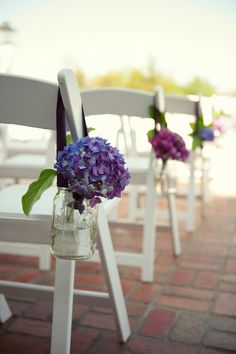 white chairs with purple and blue flowers in mason jars are lined up on the brick floor