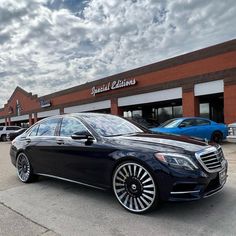 a black mercedes s - class parked in front of a car dealership on a cloudy day