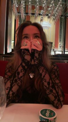 a woman sitting at a table with her hands covering her mouth and looking up to the camera