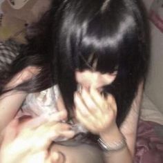 a girl with black hair is holding her hands up to her face