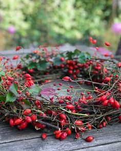 a wreath made out of branches and berries on top of a wooden table in the woods