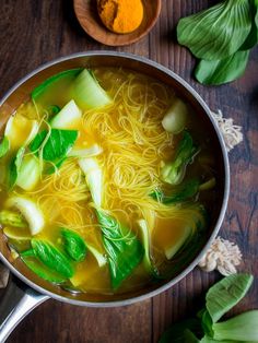 a pot filled with noodles and vegetables on top of a wooden table next to spices