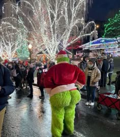 people are walking down the street with christmas lights on trees in the background and one person dressed as santa clause