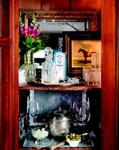 a wooden shelf filled with bottles and glasses on top of a table next to a mirror