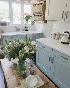 a kitchen with blue cabinets and white countertops has flowers in a vase on the table