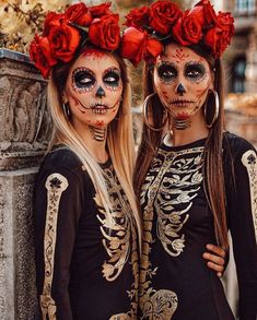 two women with skeleton makeup and red roses on their heads are standing next to each other