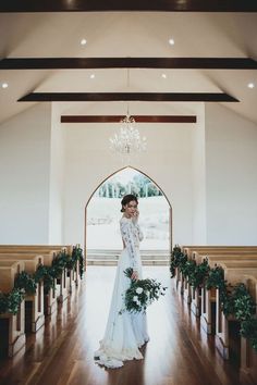 the bride is walking down the aisle with her bouquet in hand and looking at the camera