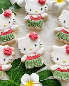 hello kitty cookies decorated with green and pink icing on a white surface next to flowers