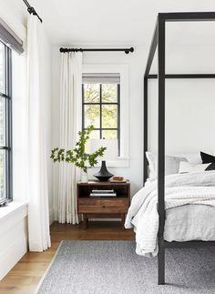 a bedroom with white walls and wood flooring has a four poster bed in the corner