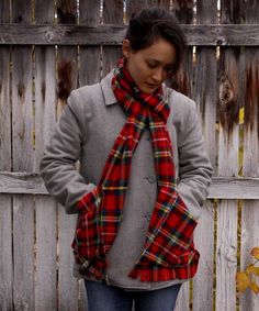 a woman standing in front of a wooden fence wearing a red and black plaid scarf