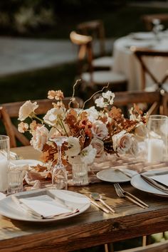 the table is set with white plates and silverware, flowers in glass vases