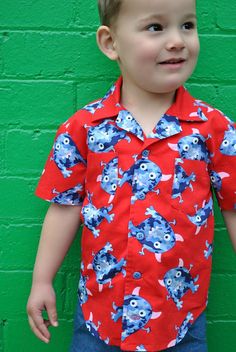 a young boy standing in front of a green wall wearing a red shirt with blue monsters on it