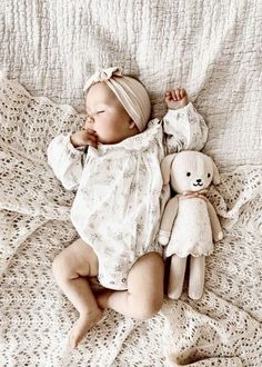 a baby laying on top of a bed next to a teddy bear