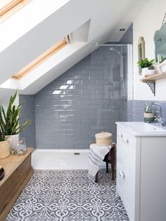 an attic bathroom with gray tile and white fixtures, including a skylight above the bathtub