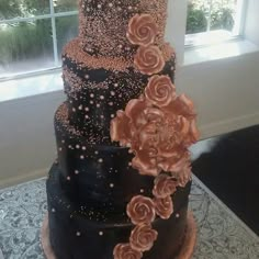 a three tiered black and gold wedding cake with flowers on it's side