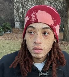 a young man with dreadlocks and a beanie looks at the camera while holding a microphone