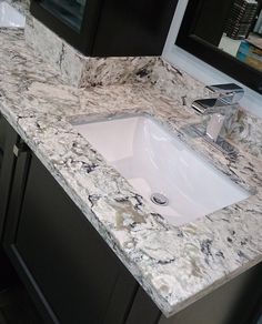 a bathroom sink sitting under a mirror next to a counter top in a room with black cabinets