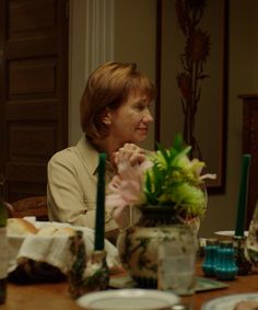 two women sitting at a table with plates and cups on it, one woman is looking off to the side