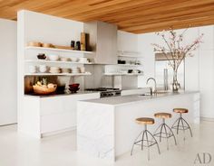 a kitchen with marble counter tops and stools in front of the island, surrounded by open shelving