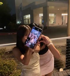 two young women taking a selfie with their cell phones in front of a building