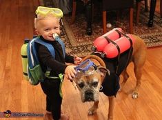 a young boy with goggles on his head standing next to a dog wearing a life jacket