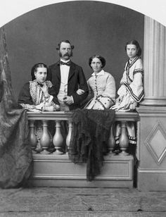 an old black and white photo of four people sitting on a bench in front of a curtain