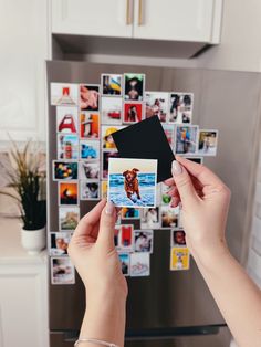 a woman holding up a polaroid photo in front of a refrigerator with pictures on it