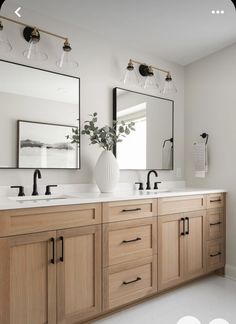 a bathroom with two sinks and mirrors on the wall, one has a vase in front of it