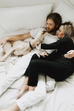 a man and woman laying on a bed with a dog in their lap next to each other