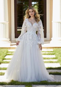 a woman standing in front of a building wearing a white wedding dress with long sleeves