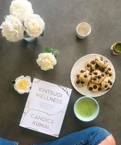 a person sitting on the floor next to a plate of cookies and a cup of green tea