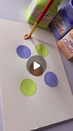 a paper with some circles on it next to paint bottles and a painting brush in the background