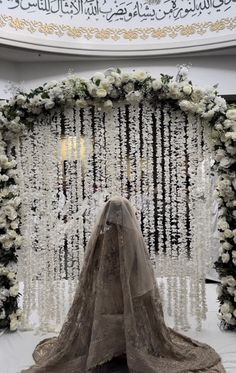 a bride's veil is draped over the back of her dress in front of an elaborate floral arch