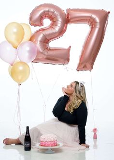 a woman sitting in front of a cake and balloons with the number twenty five on it