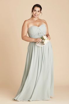 a woman in a strapless dress holding a basket and smiling at the camera while standing against a beige background