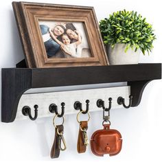 a wooden shelf with key hooks and two pictures hanging on the wall next to a potted plant