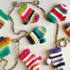 crocheted mittens and gloves hanging from chains on a white surface with other knitted items