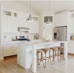 a large kitchen with white cabinets and wooden stools in front of an island counter