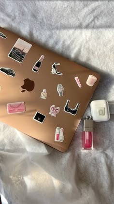 an apple laptop with many stickers on it and a lipstick bottle next to it